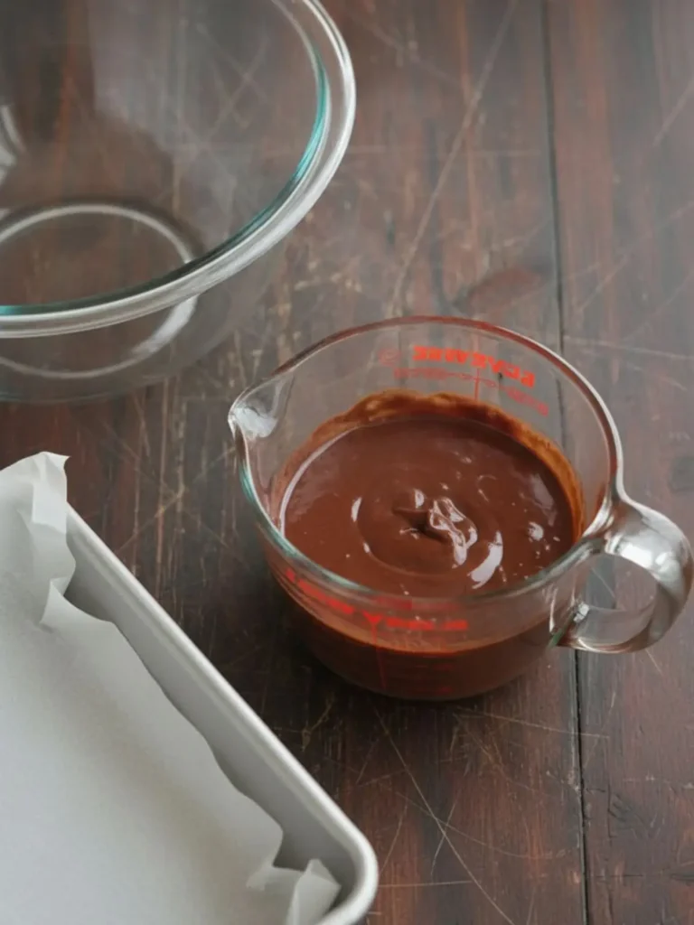 Fudgy Homemade Brownies Step 2 of seriously fudgy homemade brownies showing butter and chopped chocolate melted into a smooth glossy mixture beside the lined pan