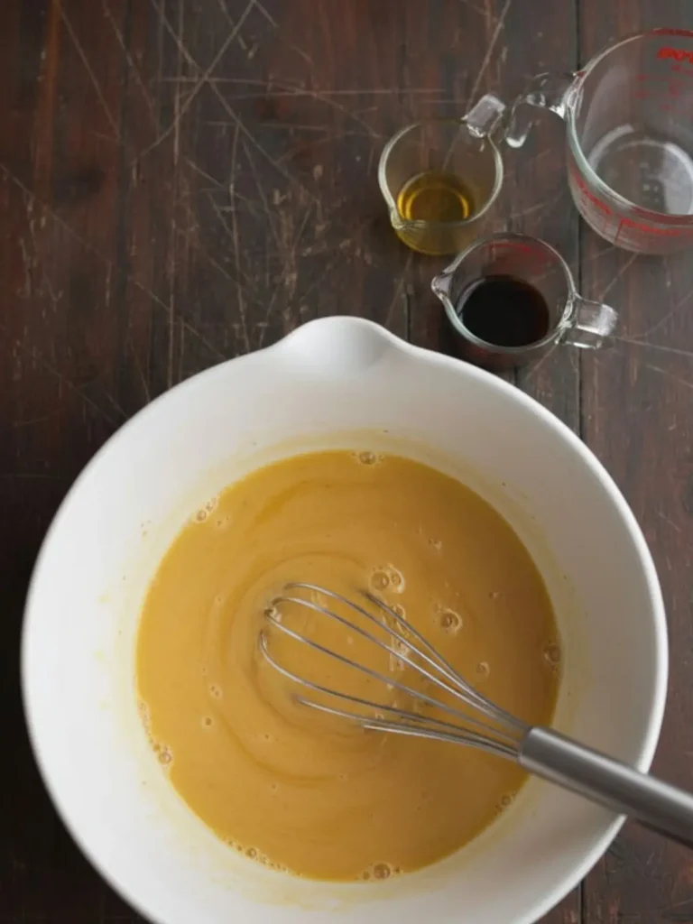 Southern Hangover Cake Whisking bourbon, oil, vanilla, and eggs together for Southern Hangover Cake to create a smooth golden liquid mixture.